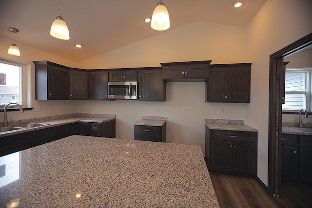 kitchen with vaulted ceiling, light stone countertops, sink, and decorative light fixtures