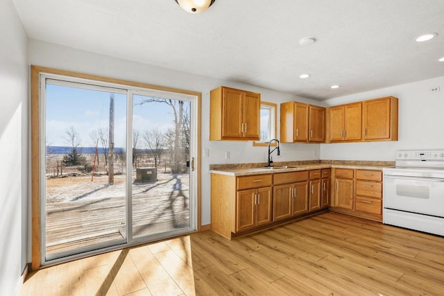 kitchen with brown cabinetry, light wood-type flooring, white electric stove, and a sink