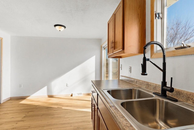 kitchen with brown cabinets, a sink, a textured ceiling, light wood-type flooring, and baseboards