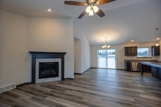 unfurnished living room with ceiling fan with notable chandelier, dark hardwood / wood-style floors, a wealth of natural light, and a tiled fireplace