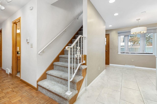 stairway featuring parquet floors and an inviting chandelier