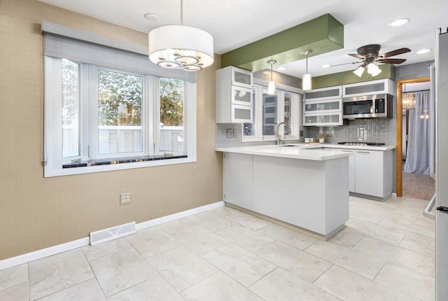 kitchen featuring sink, hanging light fixtures, tasteful backsplash, kitchen peninsula, and white cabinets