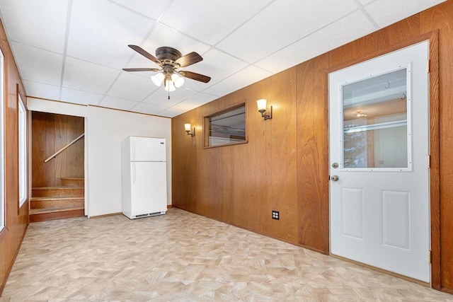 spare room featuring light parquet flooring, a drop ceiling, ceiling fan, and wooden walls