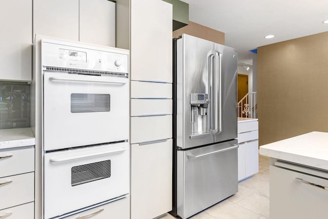 kitchen with white cabinetry, stainless steel refrigerator with ice dispenser, double oven, dishwashing machine, and light tile patterned flooring