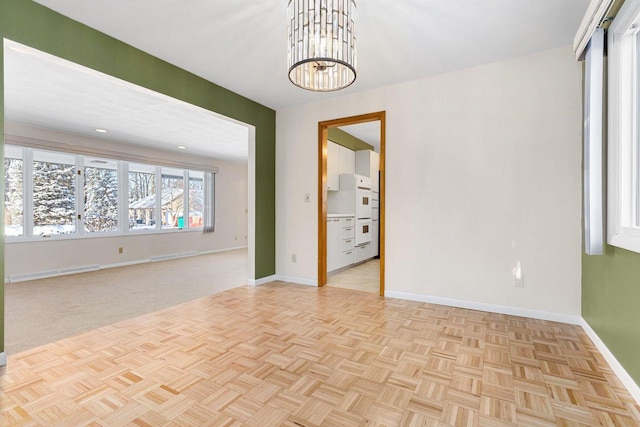 spare room with baseboard heating, light parquet flooring, and a chandelier