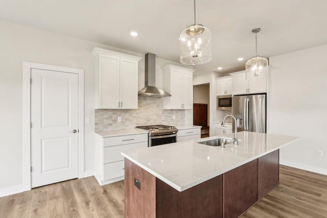 kitchen featuring appliances with stainless steel finishes, sink, white cabinets, a kitchen island with sink, and wall chimney range hood