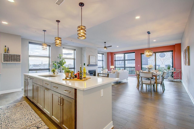 kitchen featuring ceiling fan, a kitchen island with sink, sink, decorative light fixtures, and a fireplace