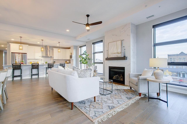 living room with ceiling fan, a large fireplace, and light hardwood / wood-style floors