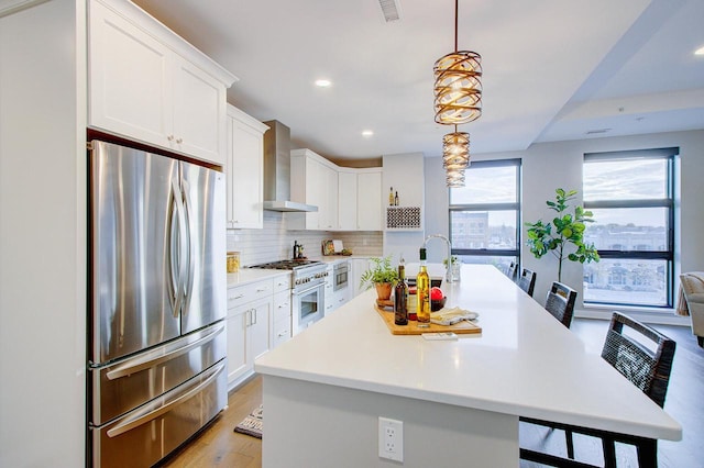 kitchen with white cabinets, a kitchen breakfast bar, wall chimney range hood, and stainless steel appliances