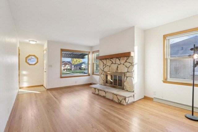 unfurnished living room with a stone fireplace, light hardwood / wood-style flooring, and a baseboard radiator