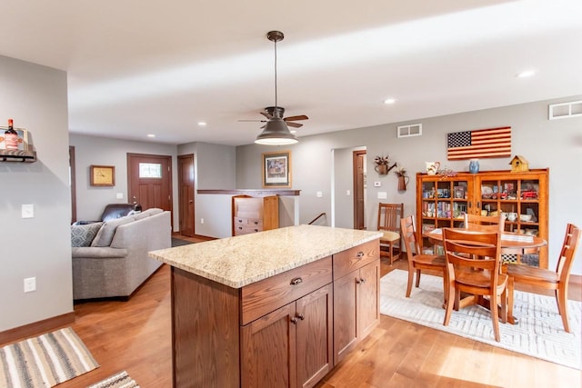 kitchen with a center island, light stone counters, light hardwood / wood-style flooring, and ceiling fan