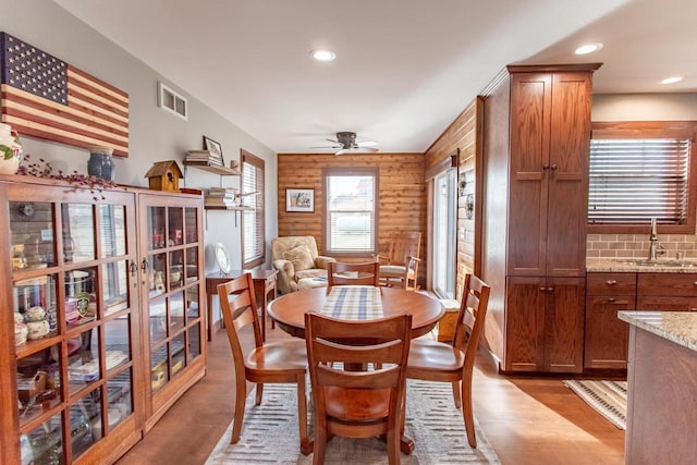 dining space with ceiling fan, sink, light hardwood / wood-style flooring, and wooden walls