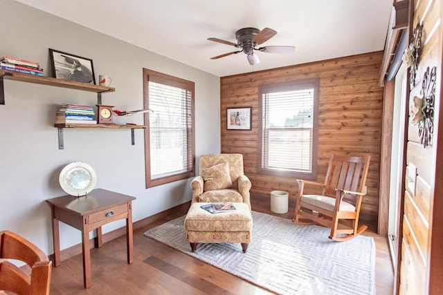 sitting room with a wealth of natural light, wood walls, and ceiling fan