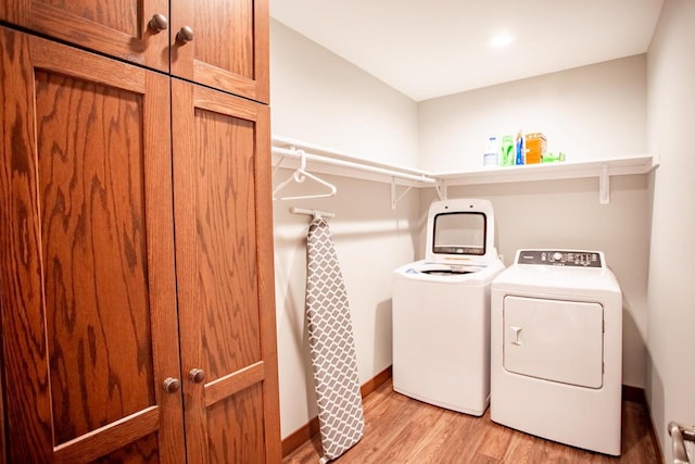 laundry area with washer and clothes dryer, light hardwood / wood-style floors, and cabinets