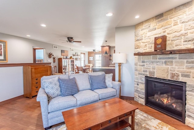 living room with a stone fireplace, ceiling fan, and light wood-type flooring