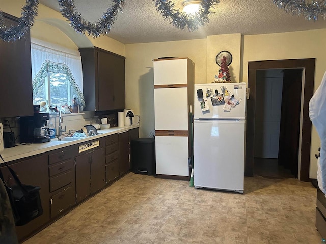 kitchen with dark brown cabinets, white fridge, a textured ceiling, and sink