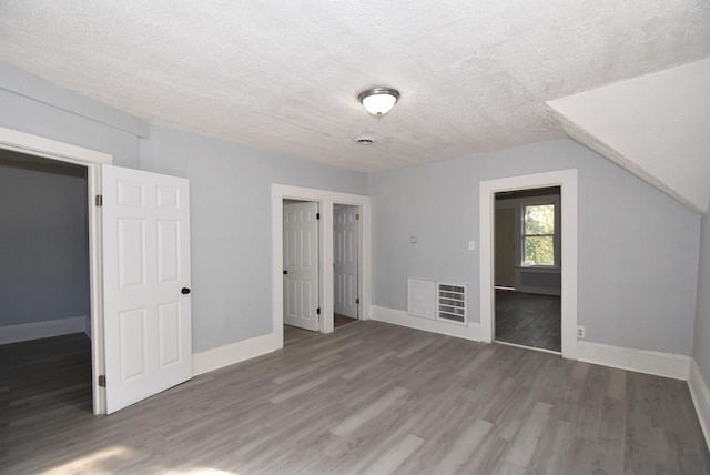 unfurnished bedroom with vaulted ceiling, dark hardwood / wood-style floors, and a textured ceiling