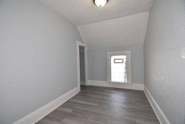 spare room with a textured ceiling, dark wood-type flooring, and lofted ceiling