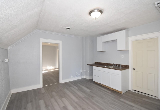 kitchen with sink, vaulted ceiling, light wood-type flooring, a textured ceiling, and white cabinetry