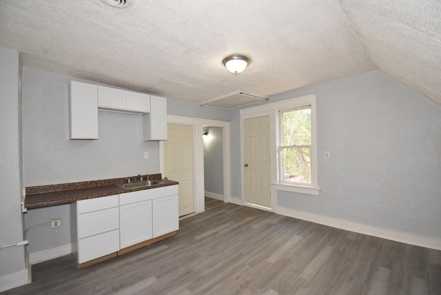 kitchen with a textured ceiling, lofted ceiling, white cabinetry, and sink