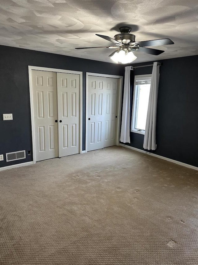 unfurnished bedroom featuring ceiling fan, light colored carpet, a textured ceiling, and two closets