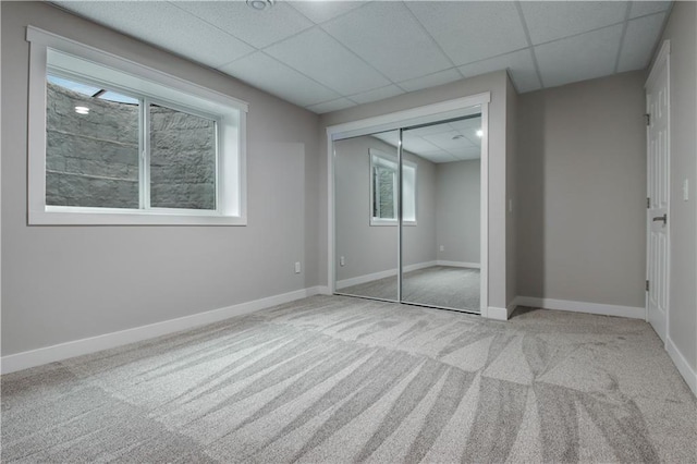 unfurnished bedroom featuring carpet flooring, a paneled ceiling, baseboards, and a closet