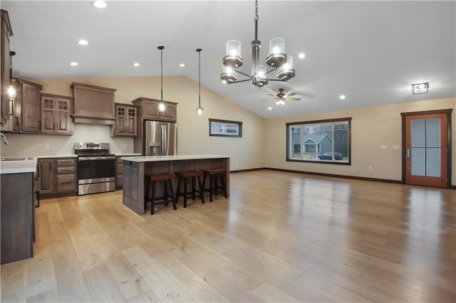 kitchen featuring a center island, ceiling fan with notable chandelier, light wood-type flooring, appliances with stainless steel finishes, and decorative light fixtures