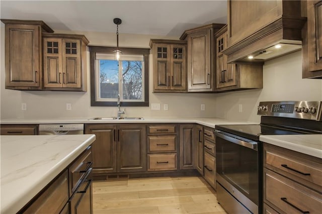 kitchen featuring light wood-type flooring, custom range hood, a sink, decorative light fixtures, and stainless steel appliances