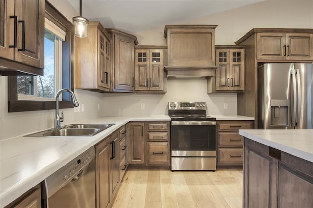 kitchen featuring custom exhaust hood, a sink, stainless steel appliances, light wood-style floors, and decorative light fixtures