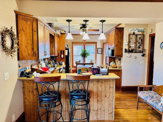 kitchen featuring kitchen peninsula, pendant lighting, light wood-type flooring, and a kitchen bar