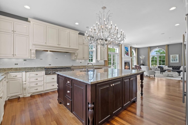 kitchen featuring a center island with sink, sink, dark hardwood / wood-style floors, dark brown cabinetry, and stainless steel gas cooktop