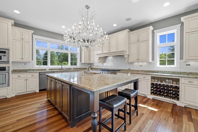 kitchen with a kitchen island with sink, sink, dishwasher, hardwood / wood-style floors, and hanging light fixtures