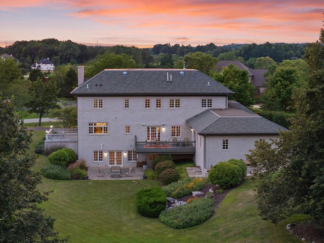 back house at dusk featuring a lawn, a patio area, and a wooden deck