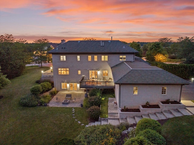 back house at dusk featuring a balcony, a yard, and a patio