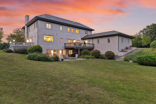 back house at dusk featuring a patio, a wooden deck, and a lawn