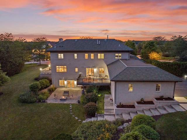 back house at dusk with a patio area, a yard, and a balcony