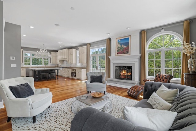 living room featuring wine cooler, a healthy amount of sunlight, light hardwood / wood-style floors, and a notable chandelier