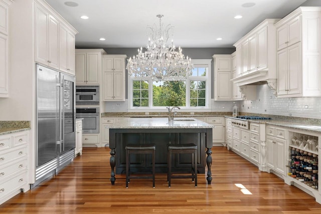 kitchen featuring a breakfast bar, a center island with sink, light stone countertops, white cabinetry, and stainless steel appliances