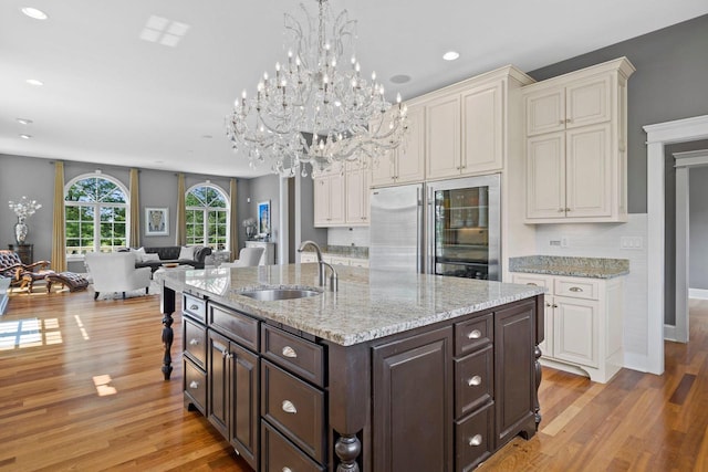 kitchen featuring sink, built in refrigerator, decorative backsplash, light wood-type flooring, and dark brown cabinetry