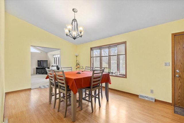 dining space with light hardwood / wood-style flooring, lofted ceiling, and an inviting chandelier