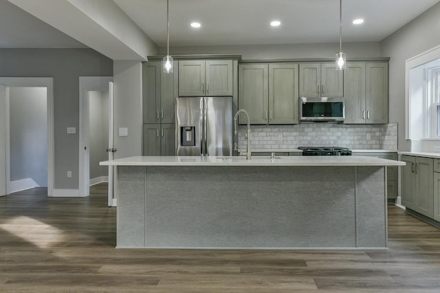 kitchen featuring decorative backsplash, stainless steel appliances, dark wood-type flooring, a center island with sink, and hanging light fixtures