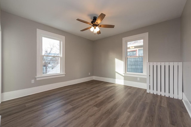 empty room with radiator heating unit, plenty of natural light, ceiling fan, and dark wood-type flooring