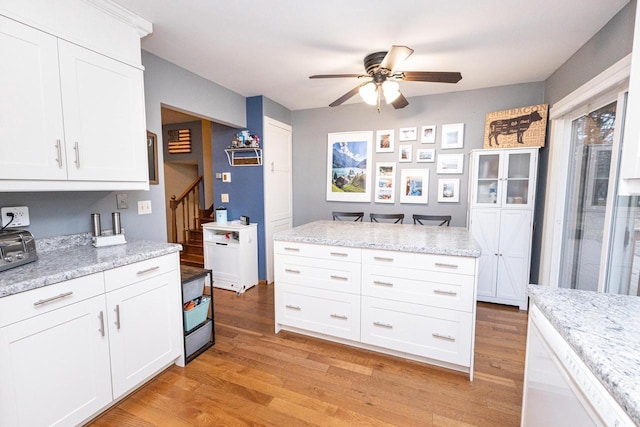 kitchen featuring light stone counters, white cabinets, light hardwood / wood-style floors, and ceiling fan