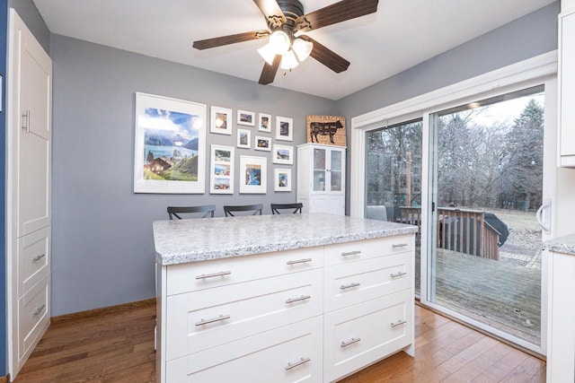 kitchen with light stone counters, a breakfast bar, white cabinets, and wood-type flooring