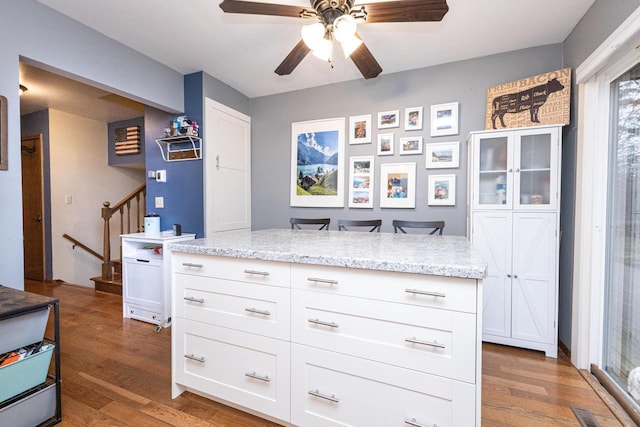 kitchen with hardwood / wood-style flooring, ceiling fan, light stone counters, and white cabinetry