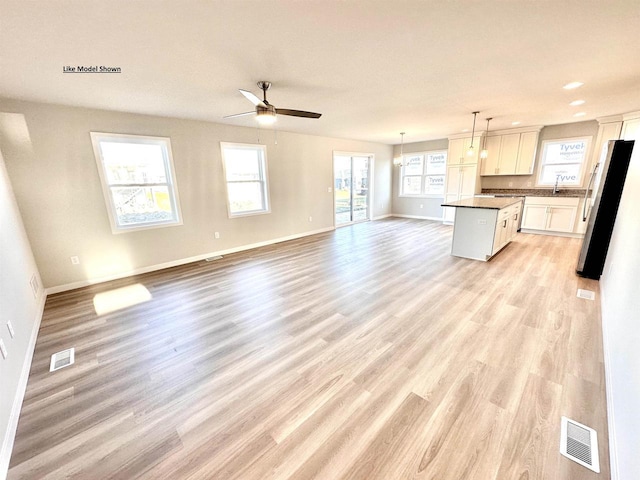 kitchen featuring white cabinets, ceiling fan, stainless steel fridge, decorative light fixtures, and a kitchen island