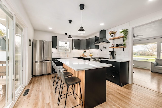 kitchen featuring pendant lighting, a center island, wall chimney range hood, a kitchen bar, and stainless steel appliances