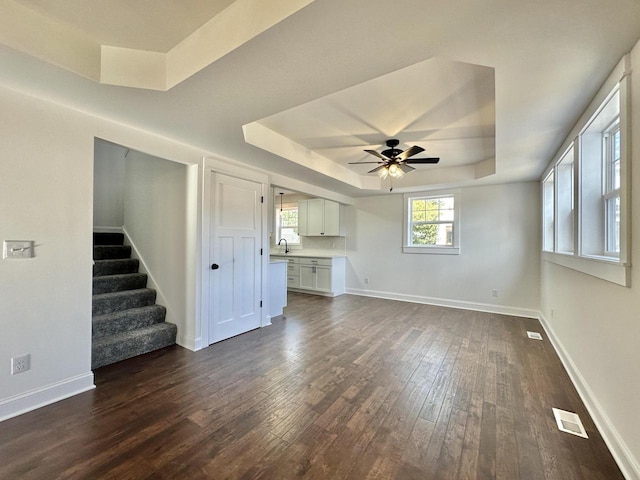 unfurnished living room with ceiling fan, dark hardwood / wood-style floors, a raised ceiling, and sink