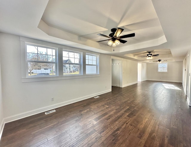 empty room with a raised ceiling, a wealth of natural light, ceiling fan, and dark hardwood / wood-style floors