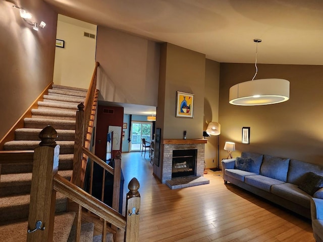 living room featuring a towering ceiling, hardwood / wood-style flooring, and a brick fireplace